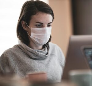 A person wearing a mask and staring at a laptop