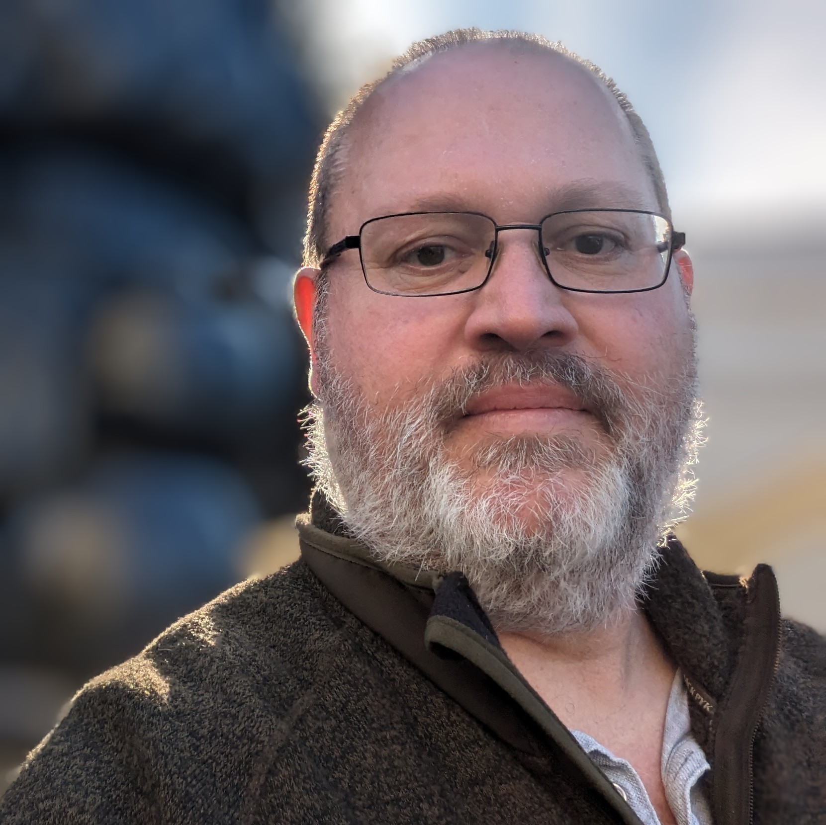 A white man with dark receding hairline cut short, wearing glasses. He has a largely white beard, though that comes and goes depending on mood.